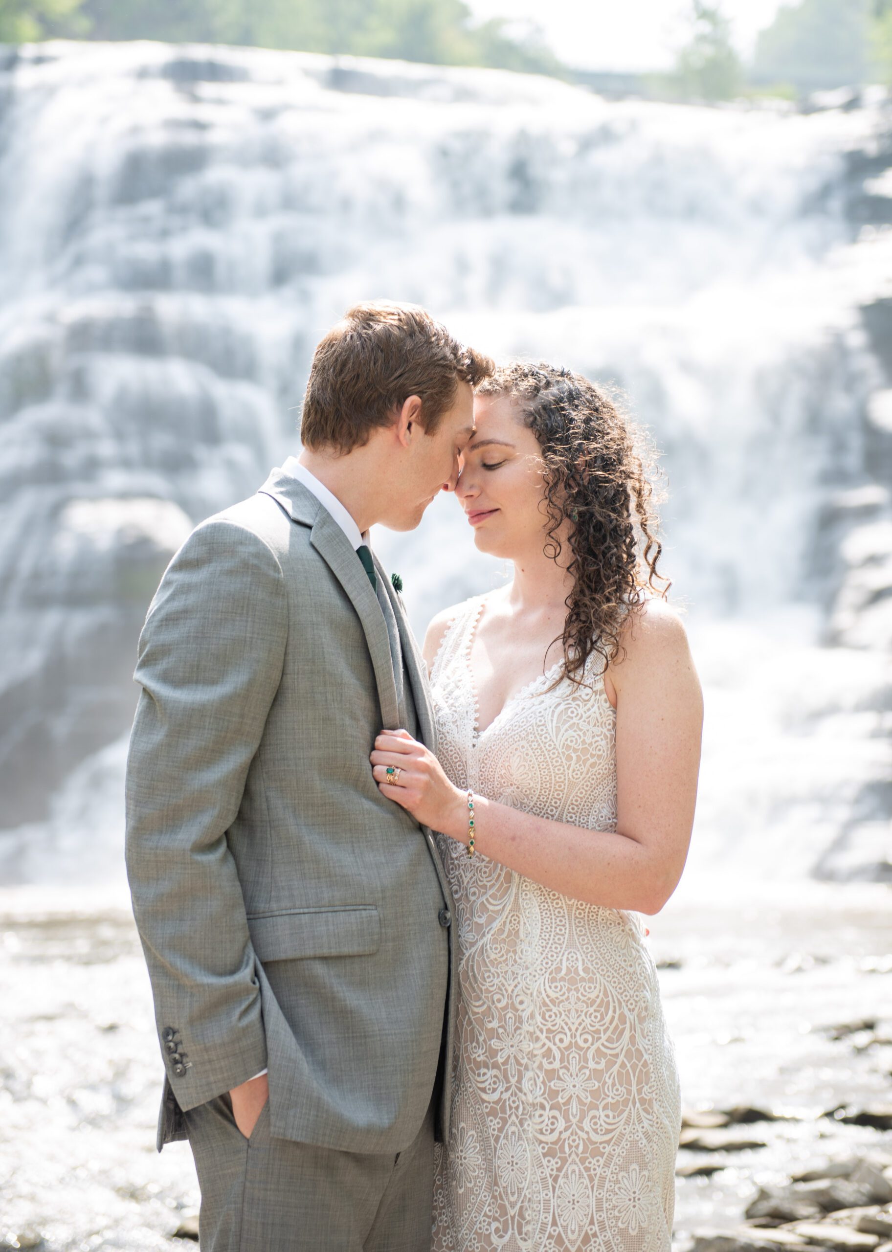 a bride and groom stand in front of an ithaca, ny waterfall in upstate ny